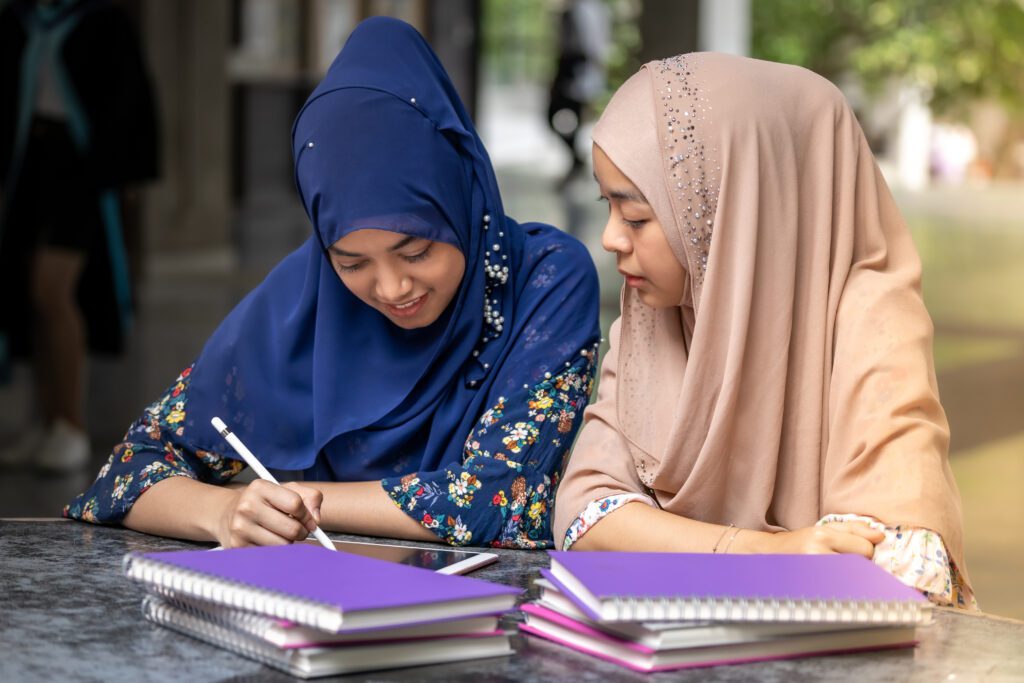 two Muslim refugee girls sitting at a table on college campus studying