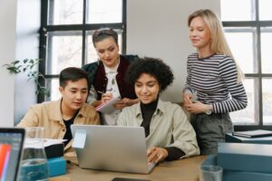 Four colleagues gathered around a laptop, talking and taking notes together — that ties to the post's theme of teams working through challenges together.