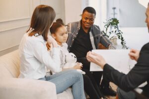 A family sits on a couch as a professional speaks with them.
