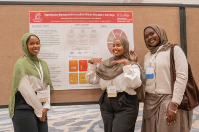 Three smiling researchers pose beside their poster on hypertension management among East African refugees in San Diego at the 2026 International Refugee and Migration Health Conference