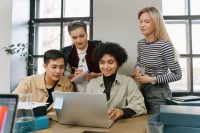 Four colleagues gathered around a laptop, talking and taking notes together — that ties to the post's theme of teams working through challenges together.