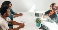 Two clients sit across a table from a service provider during a meeting.