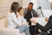 A family sits on a couch as a professional speaks with them.