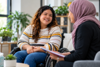 A person smiling at another person from a wheel chair.